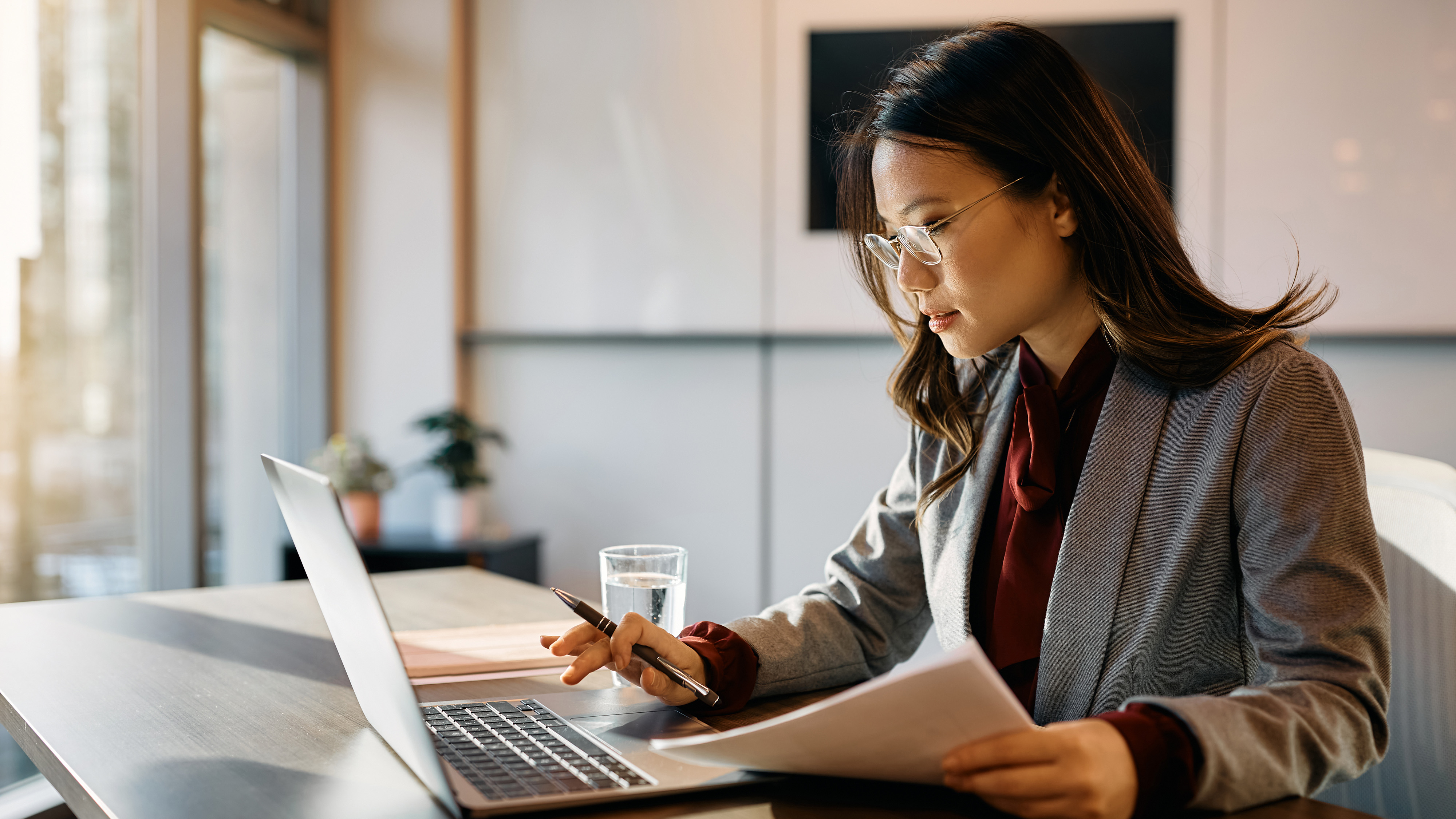 A businesswoman reviewing documents while working on a laptop in an office