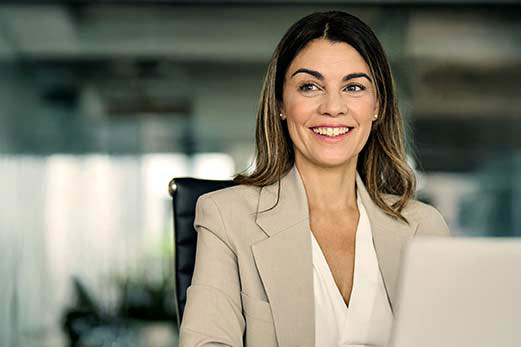 A businesswoman smiling while working on a laptop in an office