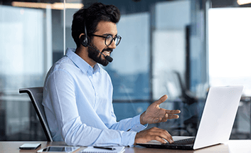 Man wearing a headset smiling while gesturing during a video call at his laptop in an office