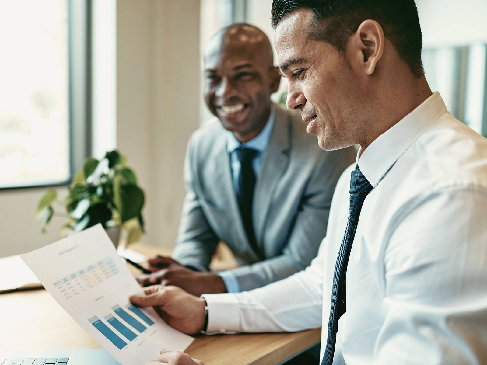 Two businessmen reviewing a printed bar chart report together in an office