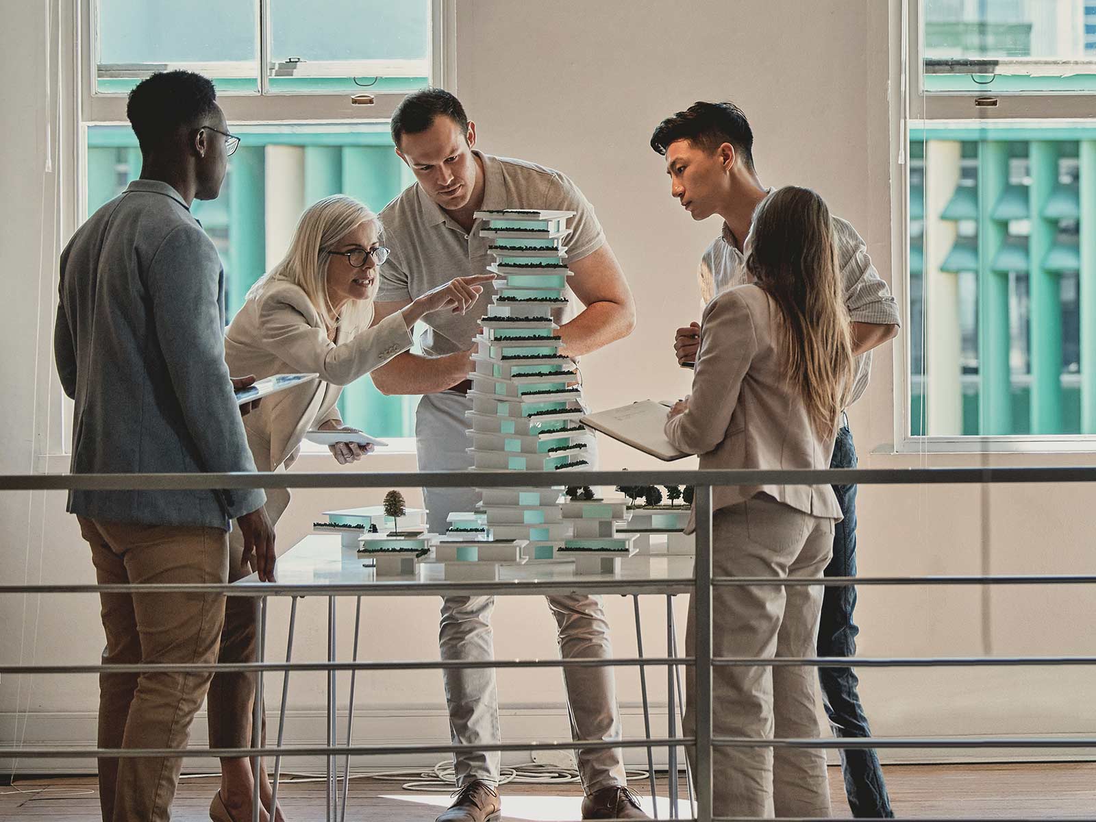 Group of five architects and planners examining a tiered scale model of a green residential tower on a table in a bright studio.