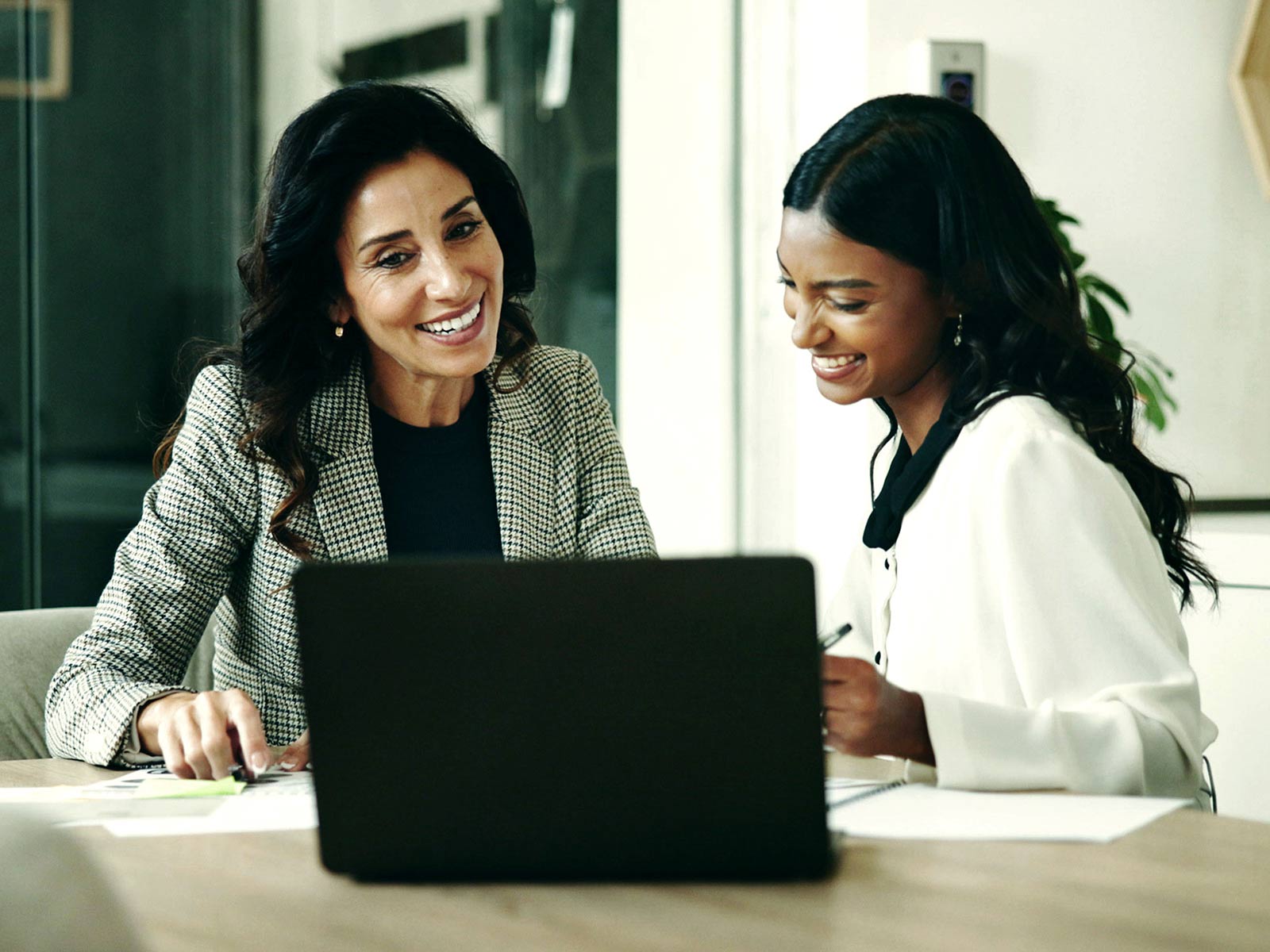 Two women smiling and collaborating over a laptop in an office