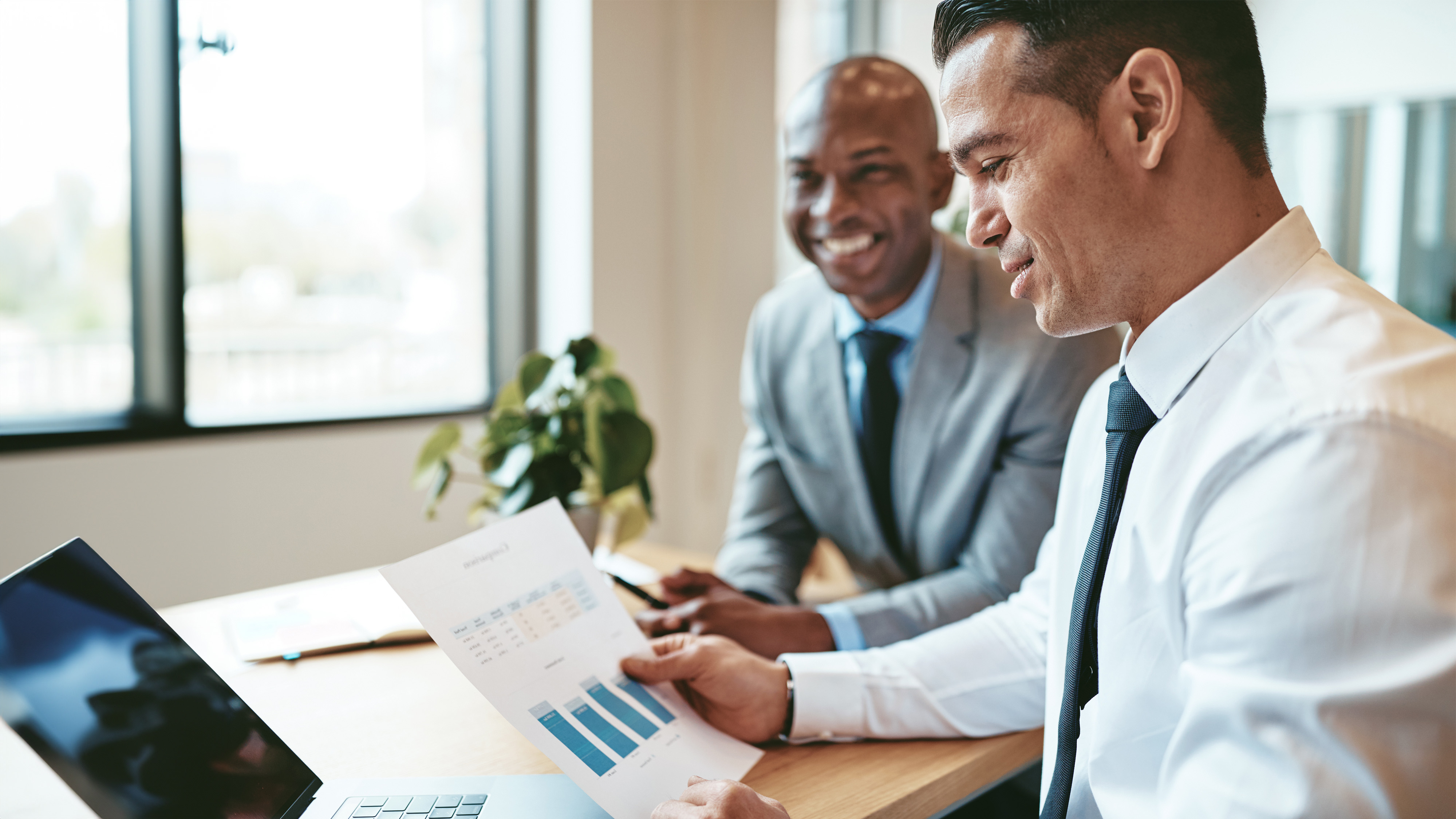 Two business professionals smiling while reviewing a document together in an office